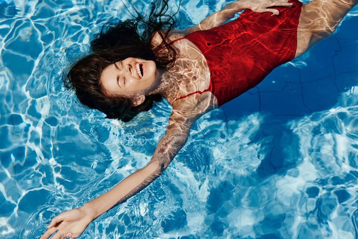 Frau in rotem Badeanzug liegt lachend entspannt auf dem Rücken im Pool und genießt das Wasser