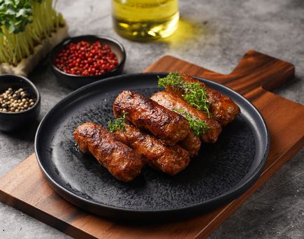 Gegrillte Cevapcici auf schwarzem Teller mit frischen Kräutern, Pfeffer und Öl angerichtet