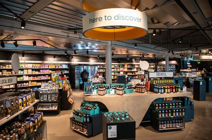 Blick in den Duty-Free-Shop am Flughafen Nürnberg mit Regalen voller Süßwaren, Getränke und regionaler Produkte sowie dem gut sichtbaren Deckenhinweis „here to discover“.