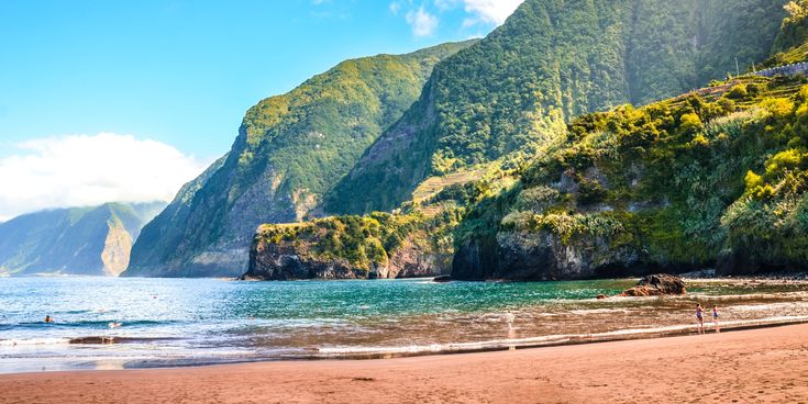 Blick auf den Sandstrand Praia do Porto do Seixal auf Madeira mit türkisblauem Atlantik, grünen Steilküsten, bewaldeten Berghängen und Badegästen an der Küste