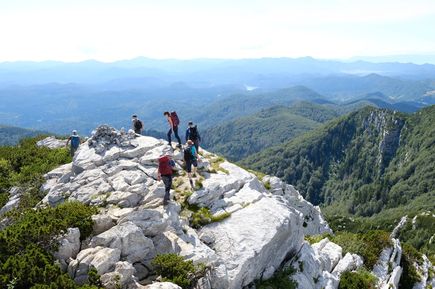 Wandergruppe im Nationalpark Risnjak in Kroatien auf felsigem Gipfel mit weiter Aussicht über bewaldete Berglandschaft