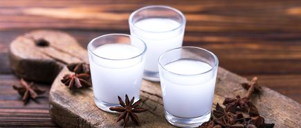Drei Gläser Rakı auf Holzbrett, milchig-weiß serviert mit Sternanis auf rustikalem Tisch