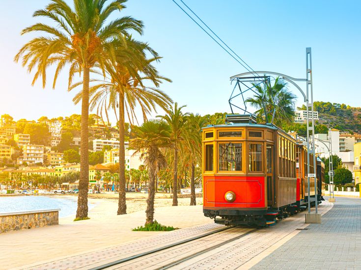 Historische Straßenbahn "Roter Blitz" in Sóller, Mallorca, mit Palmen und Stadt im Hintergrund