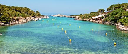 Schmale Bucht Cala Santandria auf Menorca mit türkisfarbenem Wasser, Booten und Badegästen zwischen felsigen Ufern
