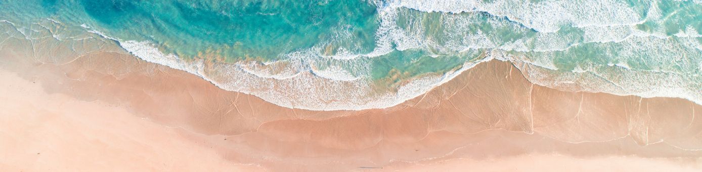 Luftaufnahme von Wellen, die sanft an einen sandigen Strand rollen