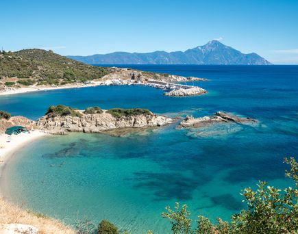 Klares blaues Wasser einer Bucht umgeben von felsigen Hügeln und grün bewachsenen Flächen an der Küste von Chalkidiki