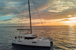 Weißer Katamaran segelt bei Sonnenuntergang auf dem Meer, der Himmel ist von Wolken und goldenem Licht geprägt