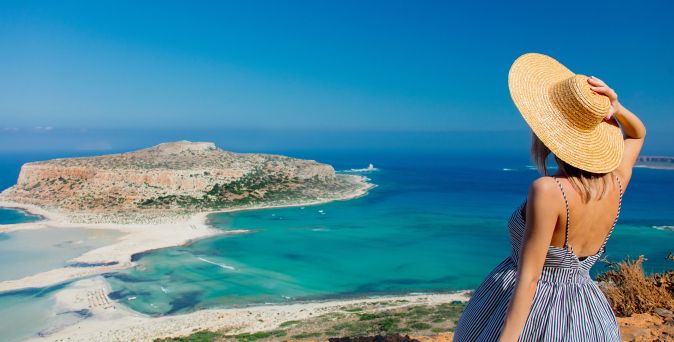 Person mit Sonnenhut blickt auf die Balos-Lagune auf Kreta in Griechenland mit türkisblauem Meer, heller Sandbank und felsiger Insel im Hintergrund