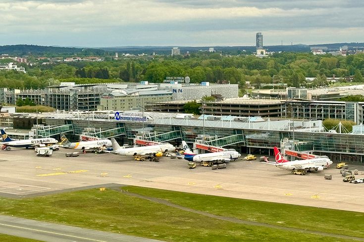 Blick auf das Vorfeld des Albrecht Dürer Airport Nürnberg mit mehreren Passagierflugzeugen an den Gates, dem Terminalgebäude und dem Stadtbild von Nürnberg im Hintergrund