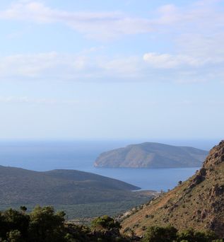 Blick auf bewaldete Hügel und Berge mit einem Inselberg im Meer unter blauem Himmel.