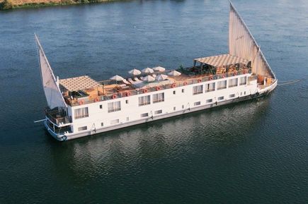 Das traditionelle Nilkreuzfahrtschiff Nile Majestic Dahabiya fährt über den ruhigen Nil, mit zwei großen hellen Segeln, Sonnendeck mit Liegen und schattigen Sitzbereichen