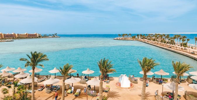 Blick auf eine Lagune mit türkisfarbenem Wasser, umgeben von Palmen und Sonnenschirmen in Ägypten