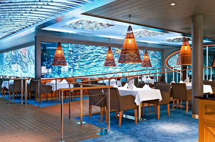 Das Ocean’s Fischrestaurant auf der AIDAcosma mit maritimem Design, gedeckten Tischen, warmen Lampen und einer großflächigen Wandgestaltung in Wellenoptik