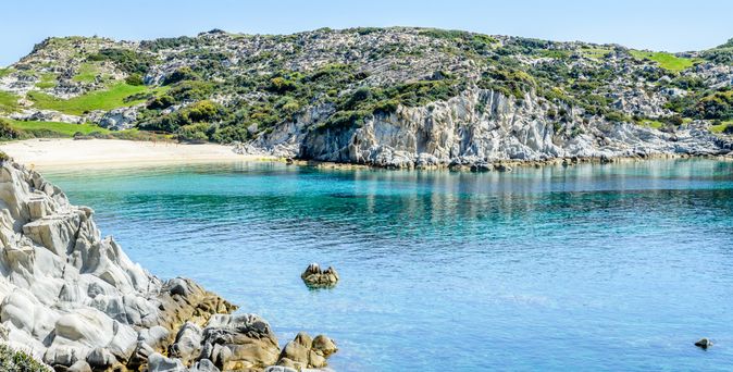 Klares blaues Meer vor felsiger Küste mit grünen Hügeln und Sandstrand in Chalkidiki