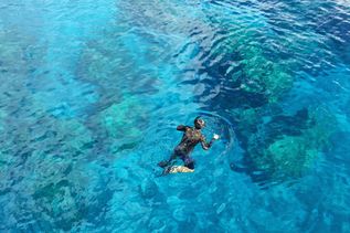 Person mit Schnorchel und Maske schwimmt auf klarem blauem Wasser über Korallenriff