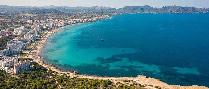 Weitläufiger Sandstrand von Cala Millor auf Mallorca mit Hotels entlang der Küste und blauem Meer