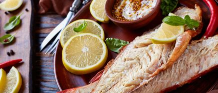 Ganze gebratene Fischplatte mit Zitronenscheiben, Chili und Kräutern auf einem Holztisch