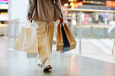 Person in heller Kleidung trägt mehrere Einkaufstüten in einem modernen Einkaufszentrum