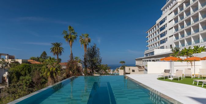 Außenpool des Hotel Atlantic El Tope auf Teneriffa mit hellen Sonnenliegen, Palmen und Blick auf die Küste in ruhiger Gartenanlage