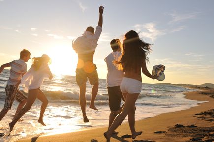 Gruppe von Menschen läuft am Strand entlang und springt über den Sand, während die Sonne im Hintergrund untergeht