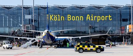 Flugzeug während der Abfertigung auf dem Vorfeld des Flughafens Köln/Bonn vor der markanten Glasfassade des Terminals mit großem Schriftzug „Köln Bonn Airport“