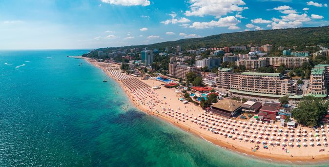 Luftaufnahme eines breiten Sandstrands in Varna mit vielen Sonnenschirmen und Hotels entlang der Küste