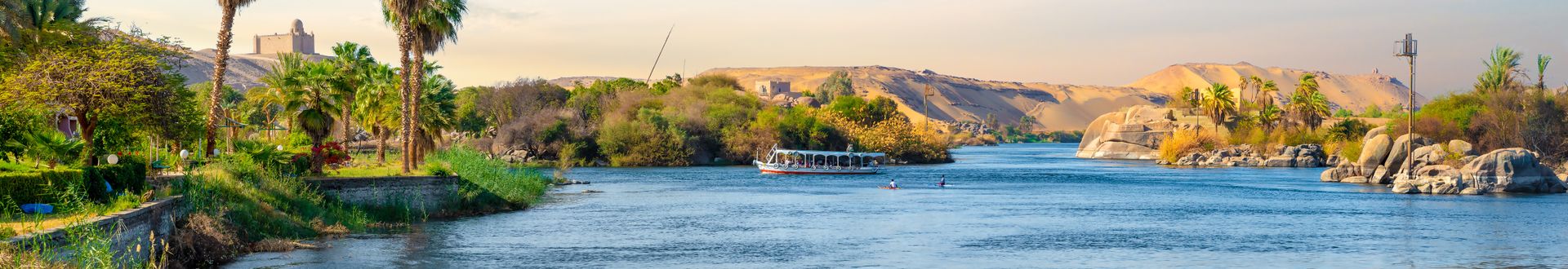 Boot auf dem Nil vor bewachsenen Ufern und Sanddünen unter blauem Himmel mit Wolken