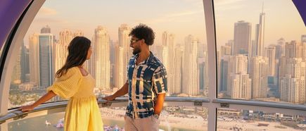 Paar steht in einer Gondel des Riesenrads Ain Dubai und blickt auf die Skyline von Dubai mit Hochhäusern und Strand im Hintergrund
