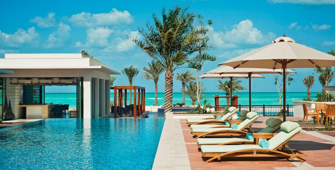 Poolbereich mit Liegen und Sonnenschirmen direkt am Sandstrand des The St. Regis Saadiyat Island Resort, Abu Dhabi, mit Blick auf das türkisfarbene Meer.