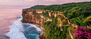Steile Küstenklippen von Uluwatu auf Bali in Indonesien mit üppiger Vegetation und Blick auf den Indischen Ozean bei Sonnenuntergang