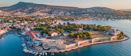 Luftaufnahme von Foça in Izmir, Türkei, mit historischem Festungswall, malerischen Häusern, Yachthafen und türkisblauem Meer vor hügeliger Landschaft