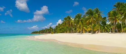 Strand mit weißem Sand und Palmen am türkisfarbenen Meer unter blauem Himmel mit Wolken