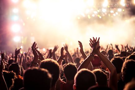 Große Menschenmenge klatscht und feiert bei einem Konzert oder in einem Club, beleuchtet von hellen Scheinwerfern