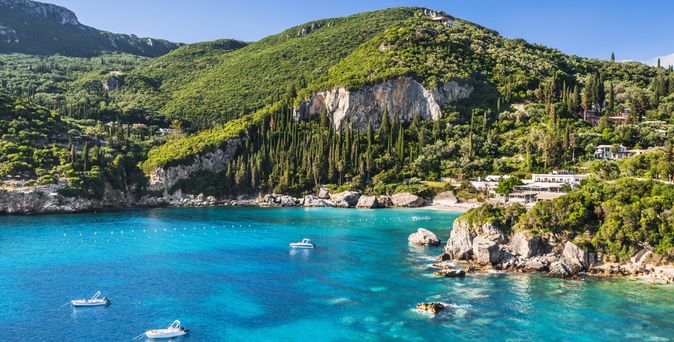 Bucht von Paleokastritsa in Griechenland mit klarem blauem Wasser, umgeben von grünen Hügeln und Felsen, zwei kleinen Booten auf dem Wasser