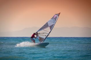 Sportler beim Kitesurfen auf dem Meer bei untergehender Sonne und Wellen
