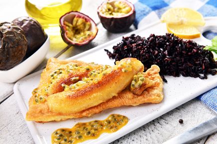 Typisches Madeira-Gericht Espada com Banana mit gebratenem Degenfisch auf knusprigem Teig, Maracuja-Sauce, schwarzem Reis und frischen Früchten auf einem Teller