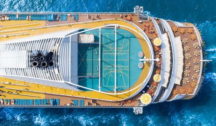 Luftaufnahme des Decks eines Kreuzfahrtschiffs mit Sportbereich, Sonnenliegen und Sitzflächen, umgeben vom tiefblauen Meer