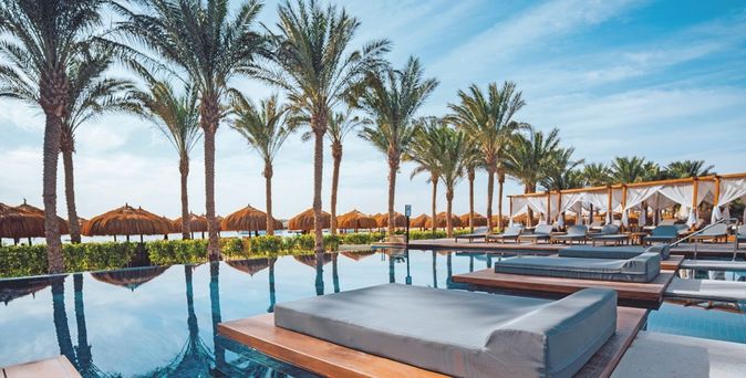 Poolbereich des Sunrise Tucana Resorts mit Liegen, Sonnenschirmen aus Stroh und Palmen unter blauem Himmel