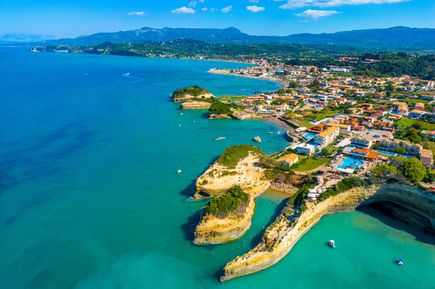 Luftaufnahme einer Küstenlandschaft mit Felsen, Stränden, Gebäuden und Bergen im Hintergrund