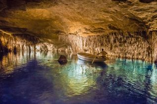 Boot fährt auf einem unterirdischen See in den Tropfsteinhöhlen Cuevas del Drach, beleuchtet von warmem Licht