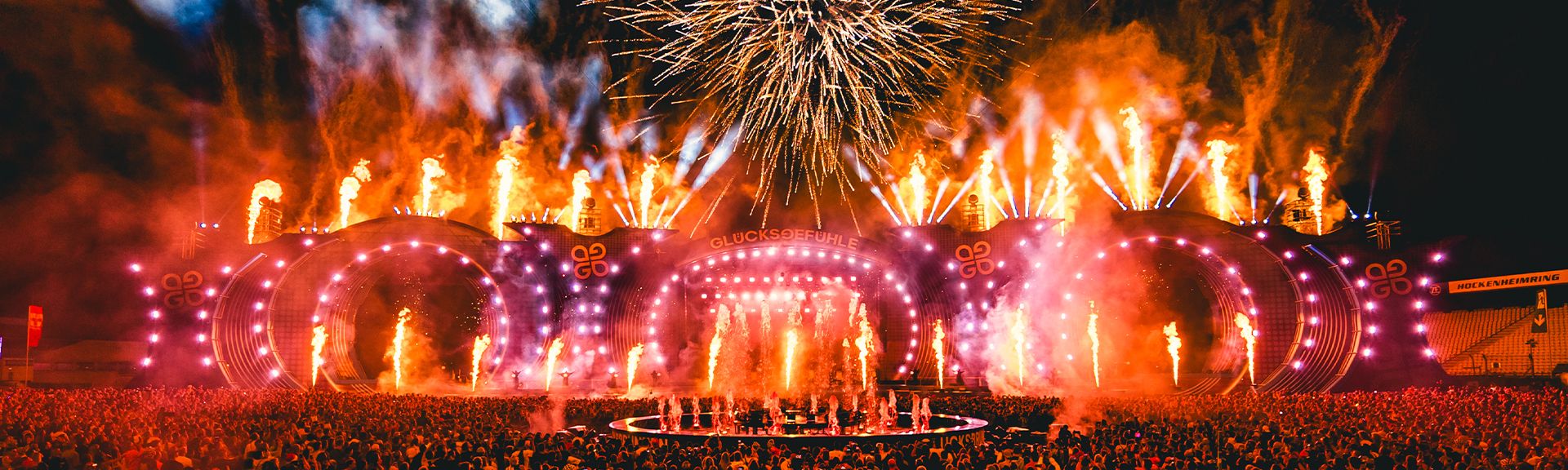 Feuerwerk und Flammeneffekte über der beleuchteten Hauptbühne des Glücksgefühle Festivals vor einer großen Menschenmenge bei Nacht.