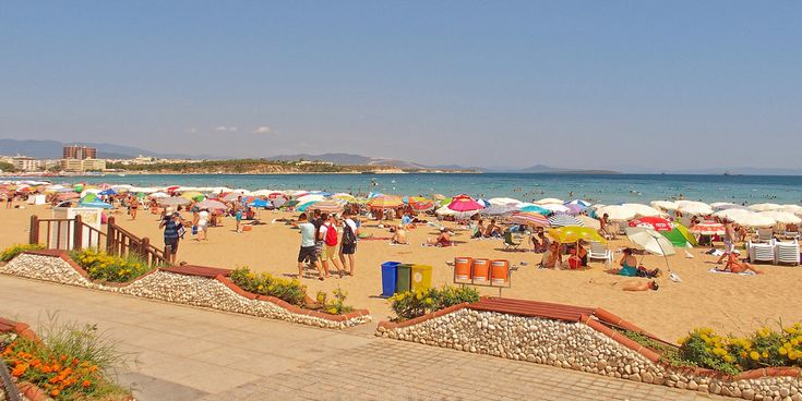 Belebter Altinkum-Strand in Didim, Türkei, mit vielen Sonnenschirmen, Urlaubern und Blick auf das blaue Meer bei klarem Himmel