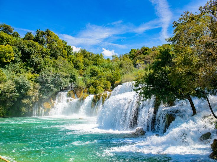 Mehrstufiger Wasserfall im Nationalpark Krka in Kroatien, umgeben von dichter grüner Vegetation und türkisfarbenem Flusswasser in einer natürlichen Landschaft.