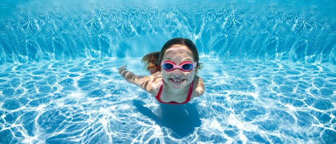 Kind schwimmt unter Wasser im Pool mit Taucherbrille