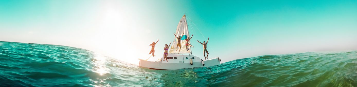 Gruppe von Menschen springt fröhlich von einem Segelboot ins Meer