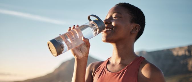 Frau trinkt erfrischendes Wasser aus einer Flasche in der Sonne nach dem Sport