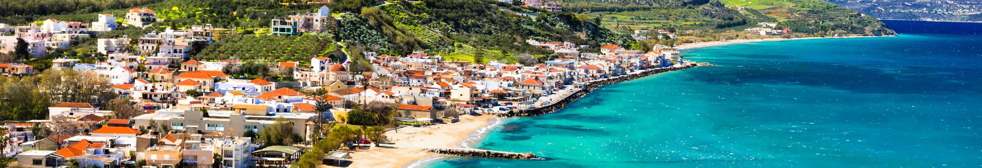 Panoramablick auf das Küstendorf Kalyves auf Kreta mit weißen Häusern, Sandstrand und türkisblauem Meer.