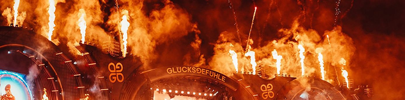 Menschenmenge beim Glücksgefühle-Festival vor einer großen Bühne mit Feuer- und Pyrotechnik-Effekten am Nachthimmel