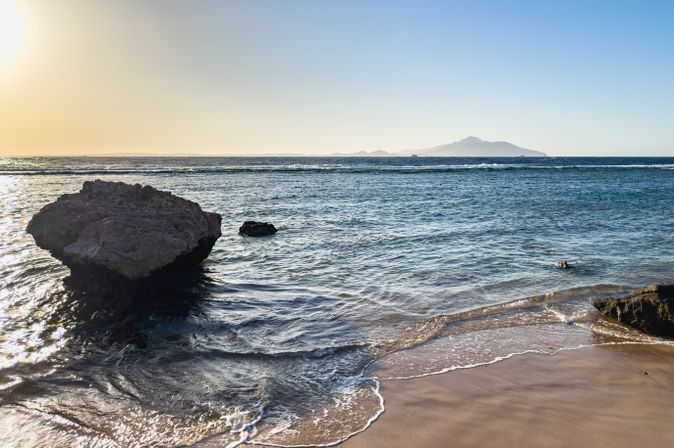 Strand mit Felsen und Blick auf die Tiran-Insel im Roten Meer in Ägypten bei Sonnenuntergang
