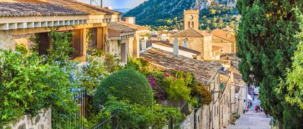 Malerische Altstadt von Pollença auf Mallorca mit engen Gassen, Blumen und Blick auf den Kirchturm